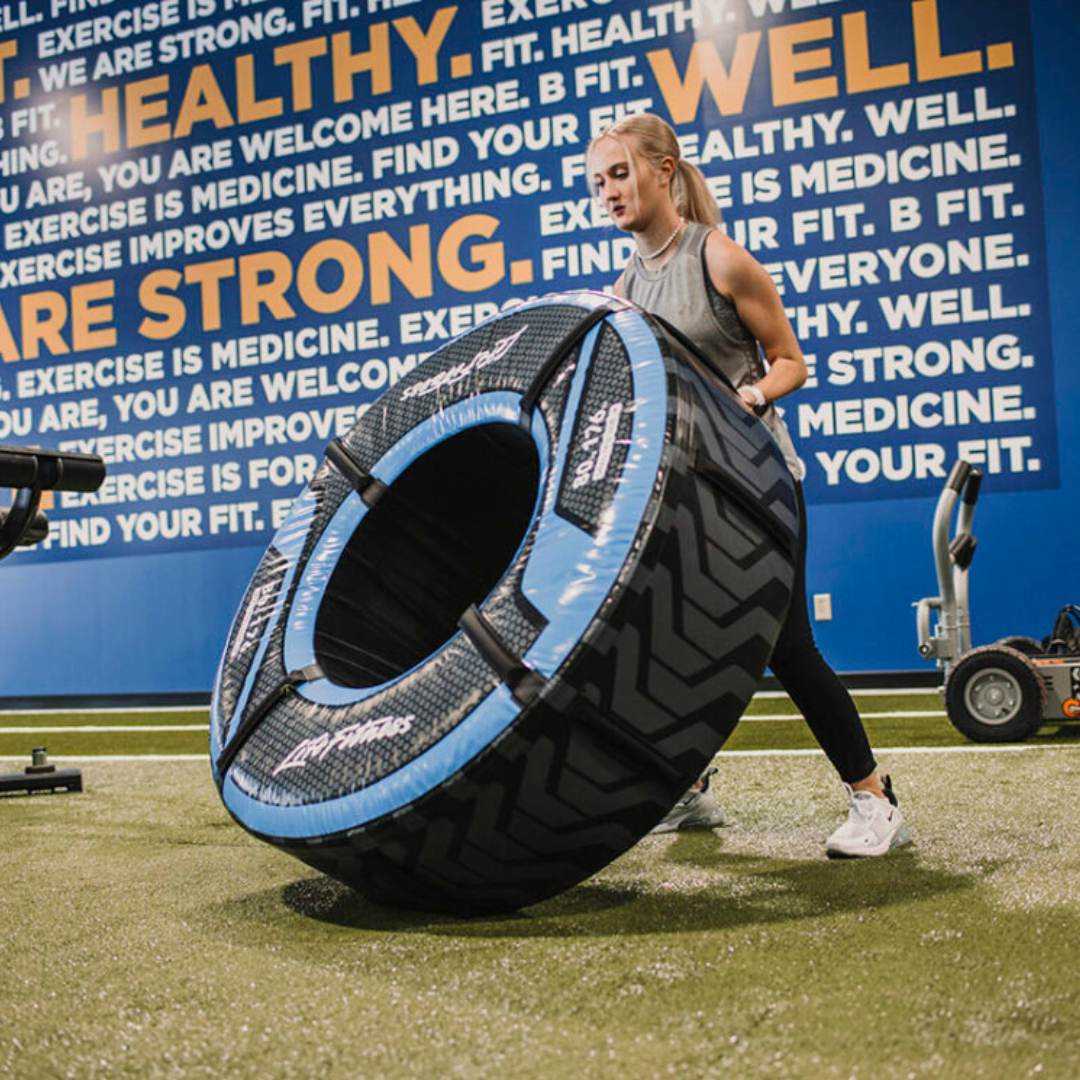 A young blonde woman flips a large tractor tire in the turf area at BFit Gym in Evansville, IN